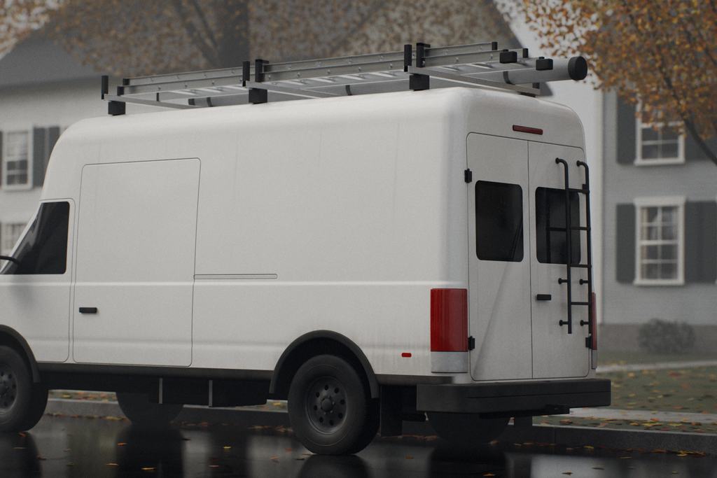 A white cargo van with a roof ladder rack parked on a wet, leaf-covered street in front of clapboard houses
